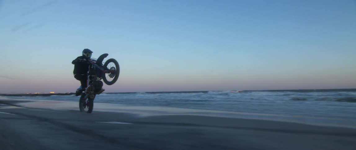 A motorcyclist does wheelies while riding along the shore of the beach