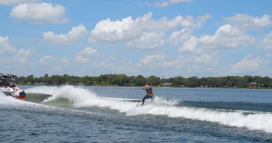 A wakeboarder spins in midair on his wakeboard while being pulled by a speeding boat on a lake during the day