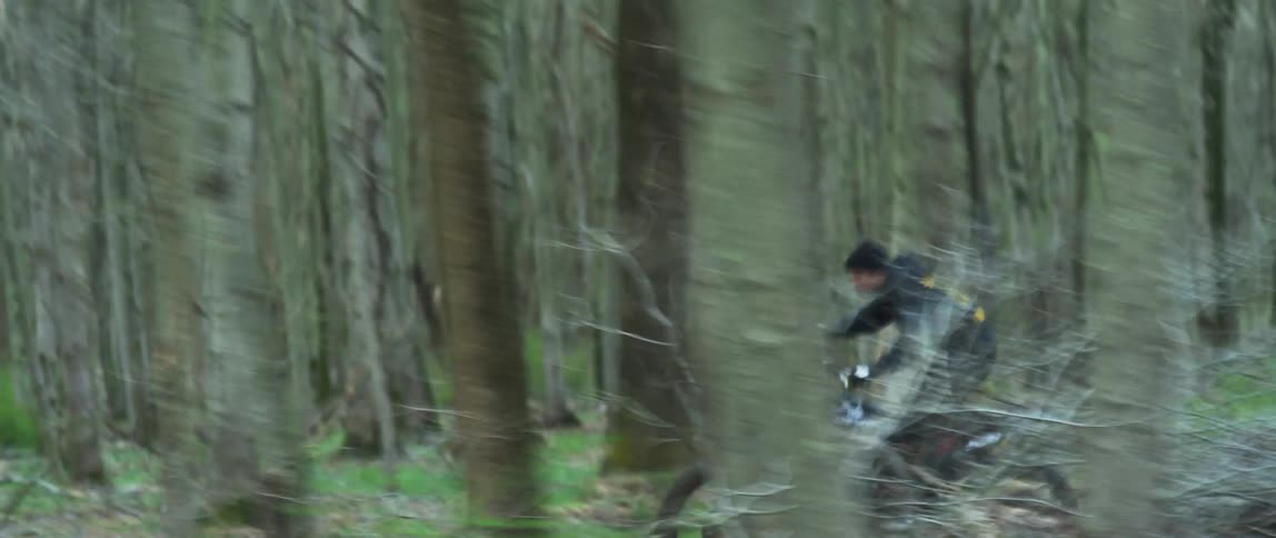 A person with a hat riding a motorcycle in a forest with trees