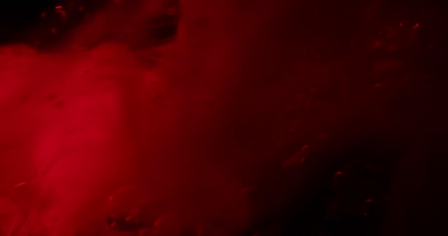 Bright red ink washing over a coral against a black background