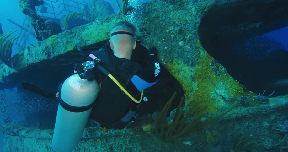 Scuba diver swimming out of a sunken ship in the blue ocean waters