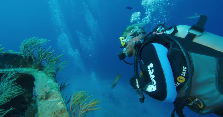 Scuba diver swimming near a sunken ship on the bottom of the ocean
