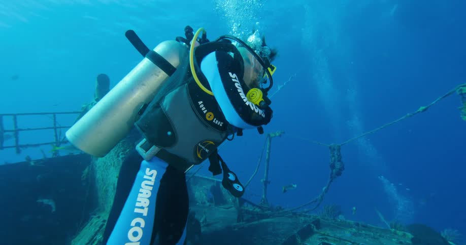 A scuba diver looks at ship wreckage under the water