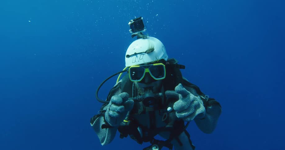A diver underwater wiggles his fingers and adjusts his mask