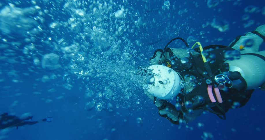 A scuba diving person breathes out air bubbles as they go underwater