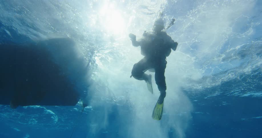 A person with scuba gear swimming underwater with bubbles next to a boat
