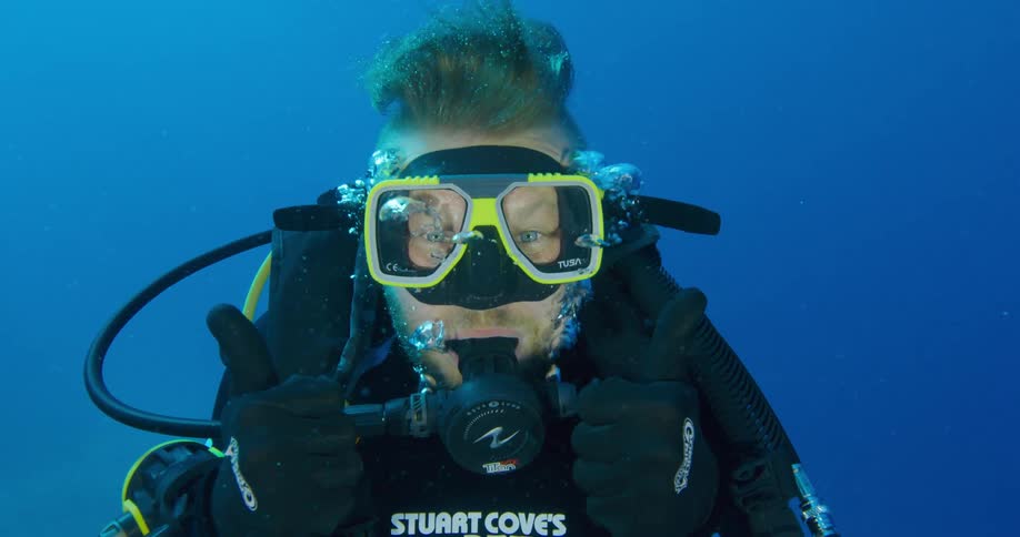 Scuba diver swimming on the blue ocean waters gives thumbs up