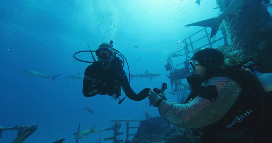 A diver hands off a camera to another diver below