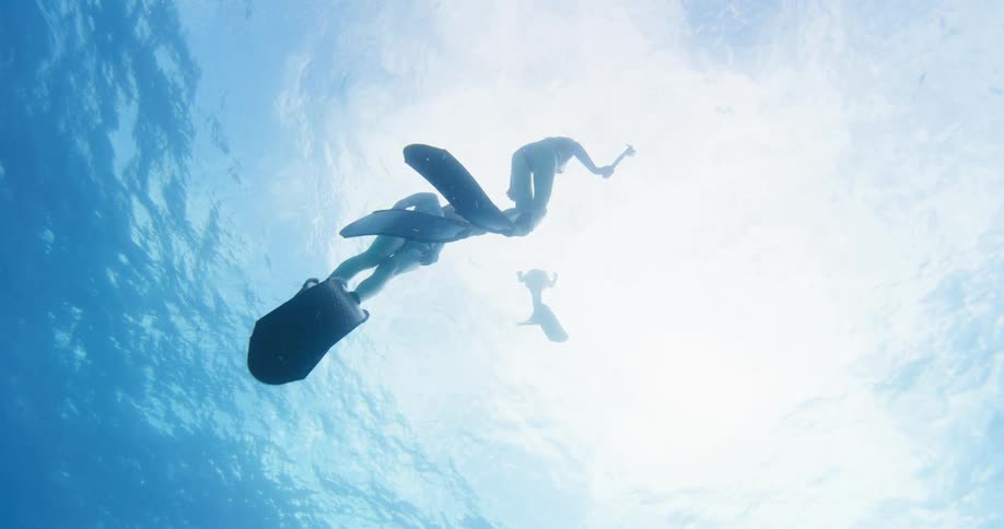 Three women with snorkels and flippers swimming underwater with the sky and clouds above