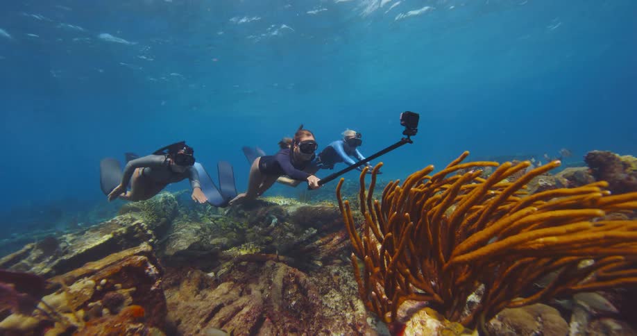 Trio of female freedivers swimming over a coral reef in the blue ocean water
