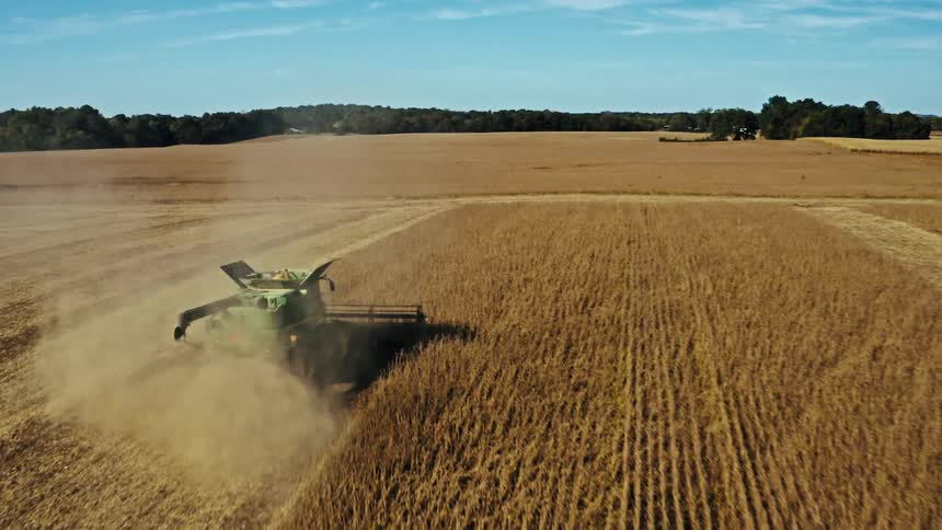 A tractor is cutting crops on farm land during the day