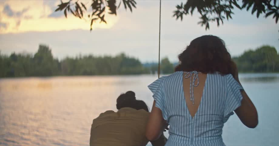 A man and woman by a lake with trees the sky and clouds in the background
