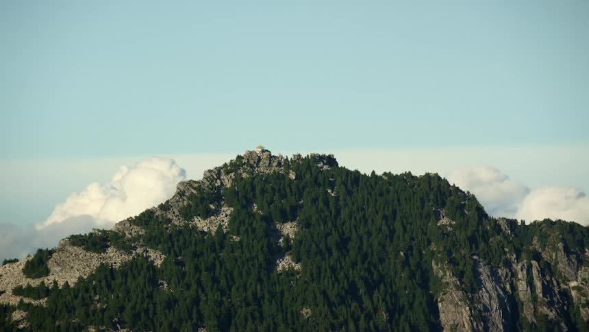An aerial shot of clouds moving behind a tall mountain