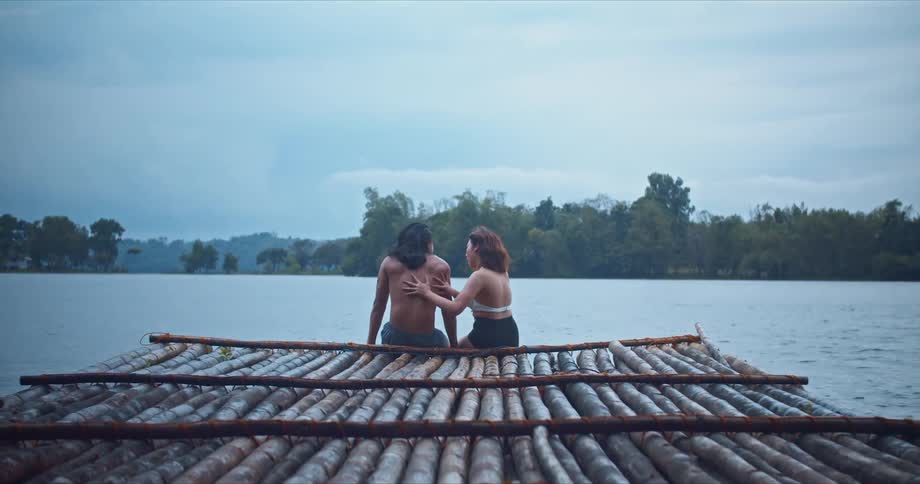 A woman pushes her boyfriend into a lake as they sit on the edge of a pier