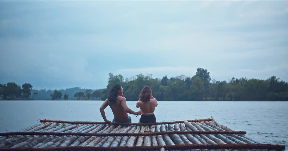A man and woman sit together on a riverside pier