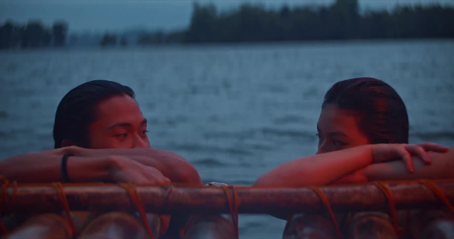 Young couple swimming on a lake reclined on the edge of a bamboo raft