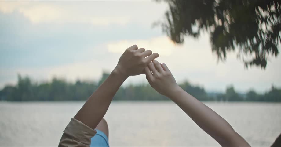 A man and a woman laying by a lake with trees the sky and clouds in the background