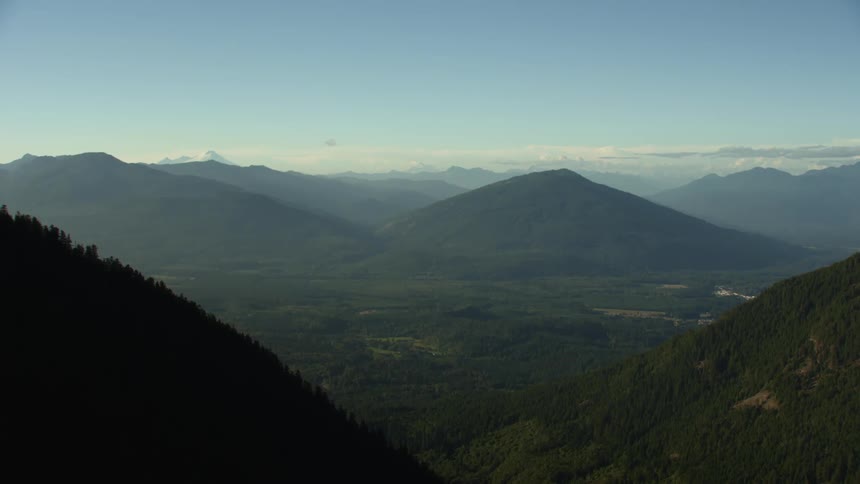 Rural valley with mountains covered with trees and peaks high in the sky