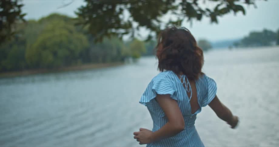 A man and a woman running by a lake with trees the sky and clouds in the background