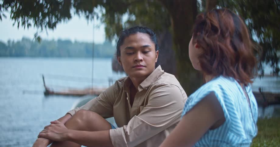 Two friends sitting on the shore of a lake talking at daytime