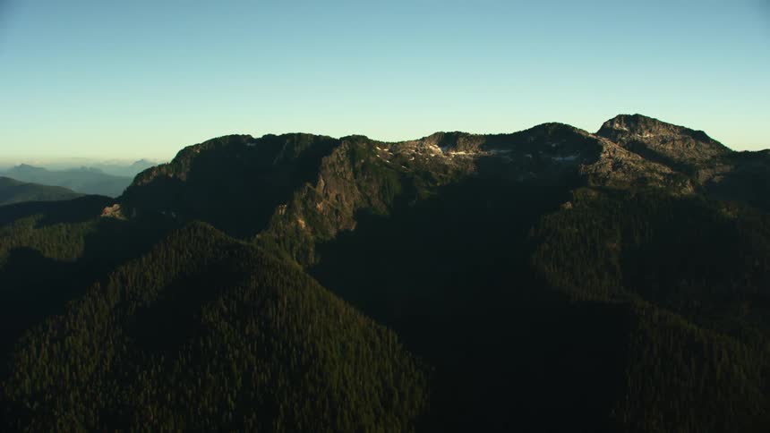 A mountain ridge covered in dense forest under a clear blue sky