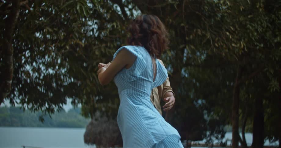A smiling man and woman dance together on a lake shore during the day
