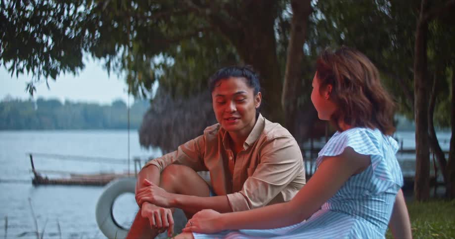 A teenage boy and girl sit on the shore and talk and laugh