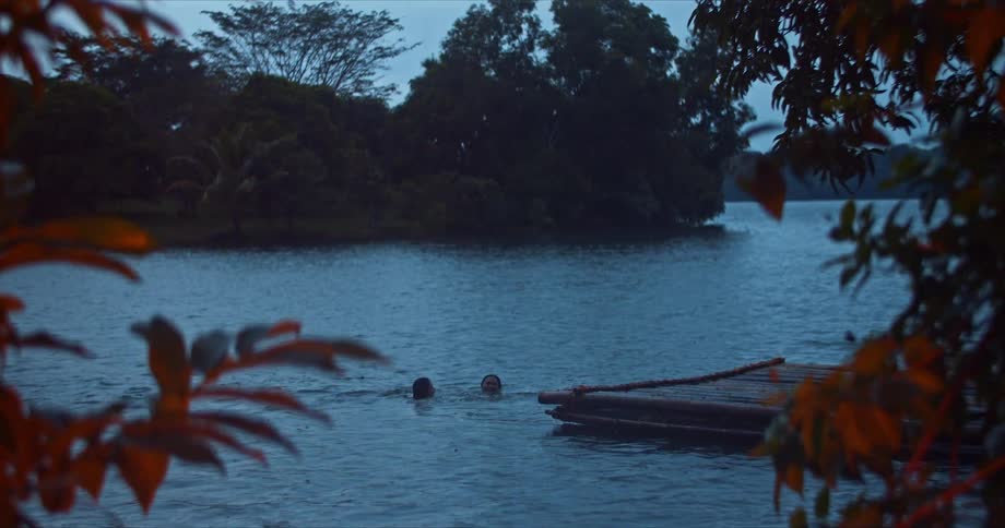 Two people tread water together near a lakeside pier