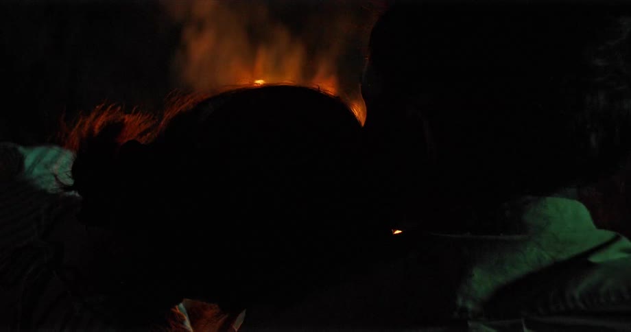 Couple lean their heads together sitting outside at night near campfire