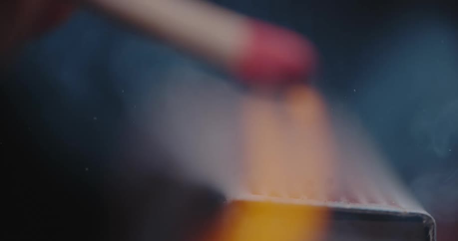 A hand strikes a match and it lights with bright yellow flame and smoke