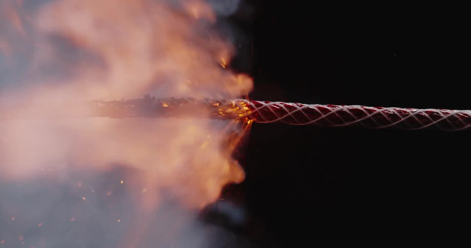 A lit wick sparks as it burns in flames and smoke