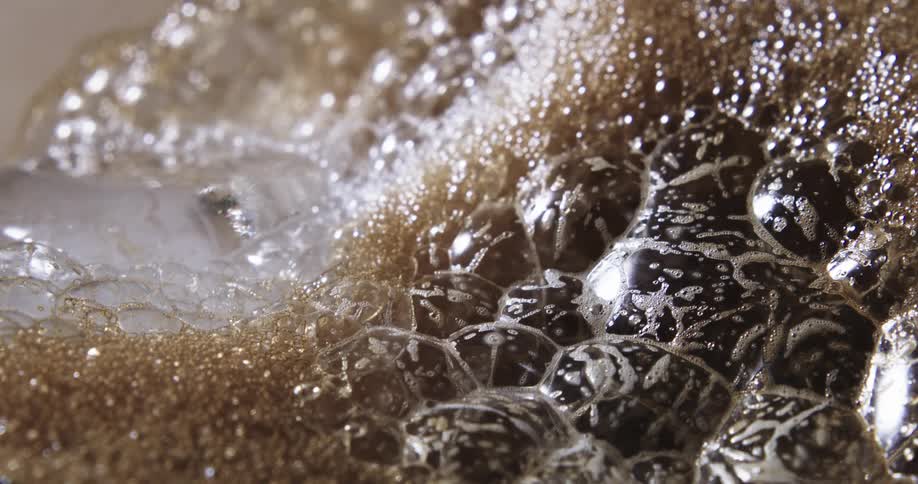Dark brown and golden brown bubbles coated in foam glisten reflecting light