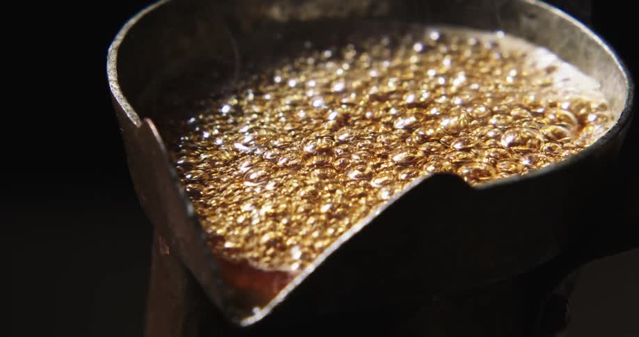A brown liquid in a metal cup is heated which makes it vigorously boil and bubble