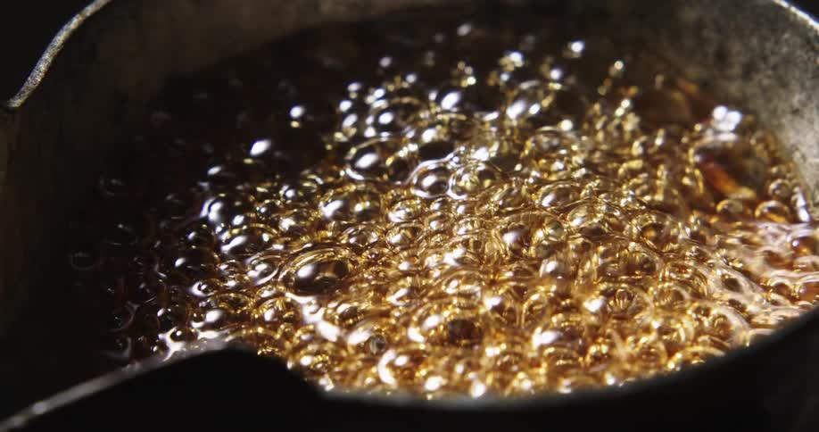 A golden brown liquid boils and bubbles in a metal pot