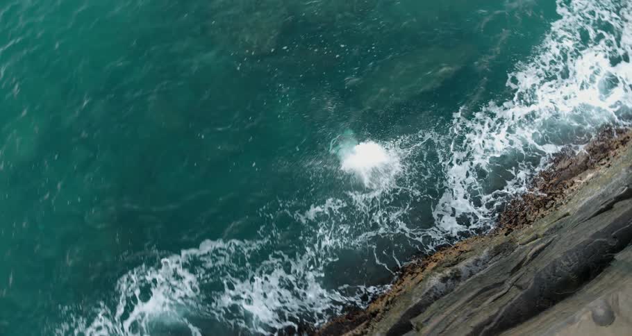 Aeria view of a man jumping into the ocean from a cliff