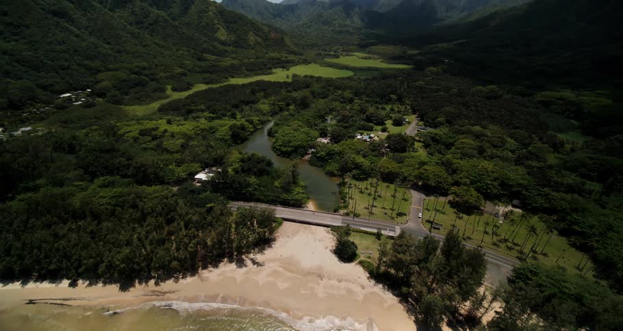 A river runs through a lush green canyon and under a bridge that leads to a beach