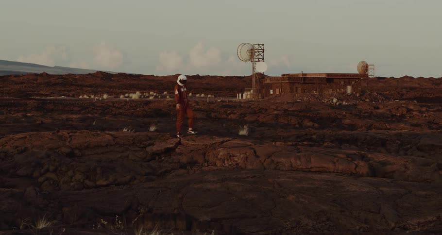A person in a space suit walks over craters and looks around