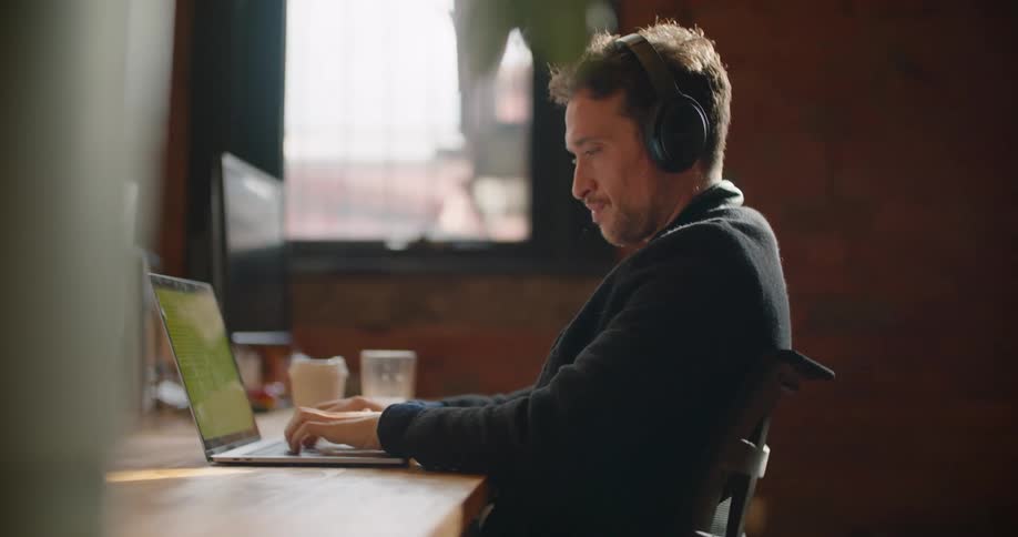 Man sitting at desk holding multiple computer monitors types on laptop