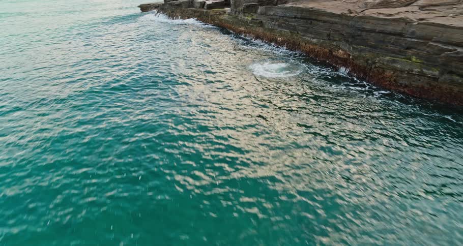 Man wearing shorts jumps into the ocean from a cliff