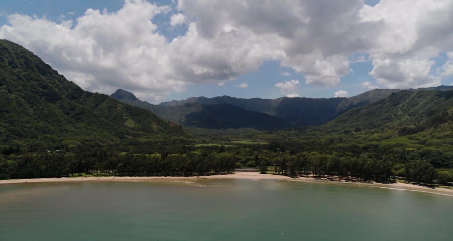 A thin strip of beach sits between the ocean and a greenery covered mountain range