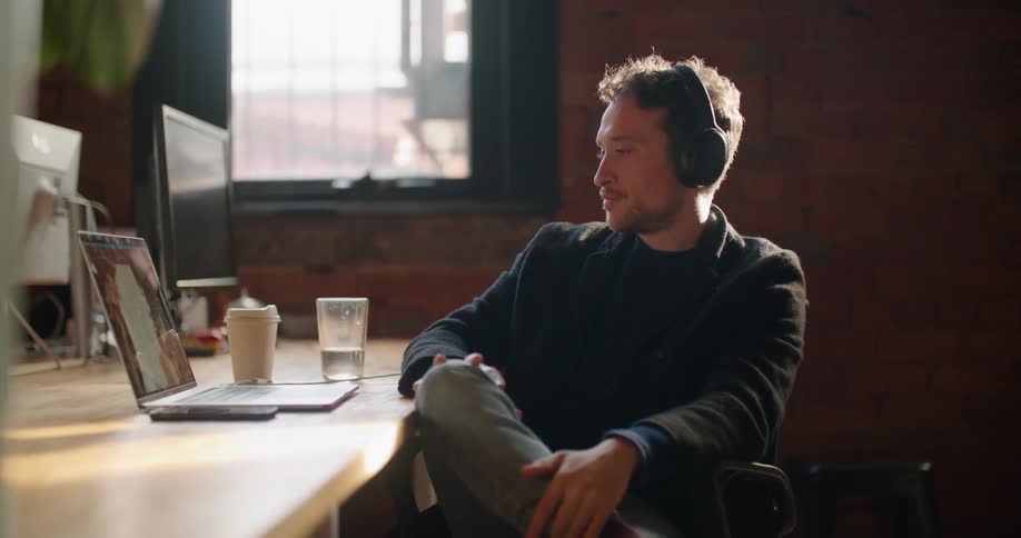 Man wearing headphones sitting in front of a laptop talks on a video conference