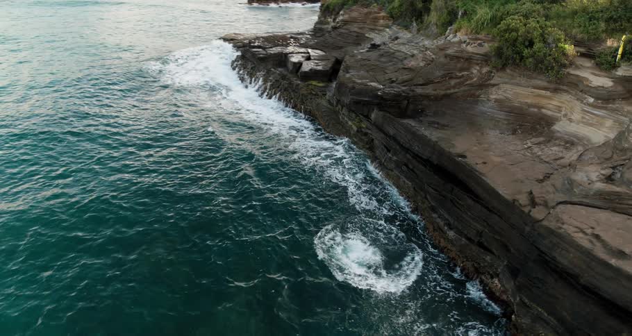 A man in swim trunks dives off a cliff and flips in the air before entering the ocean below