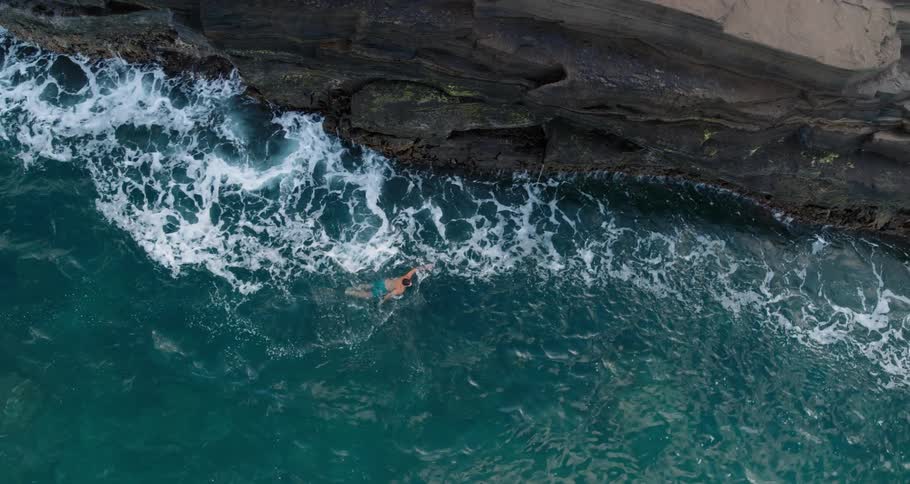 Man swimming on the green ocean waters near a rocky cliff