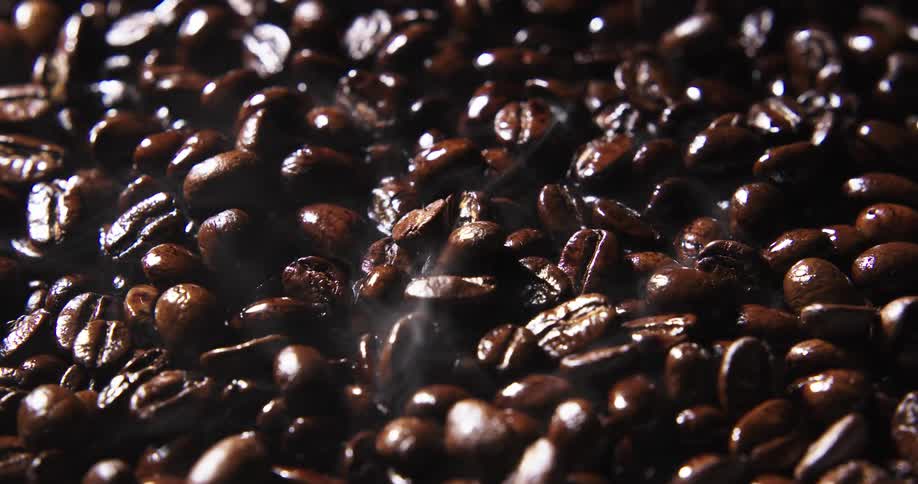 Steam rises from dark brown roasted coffee beans