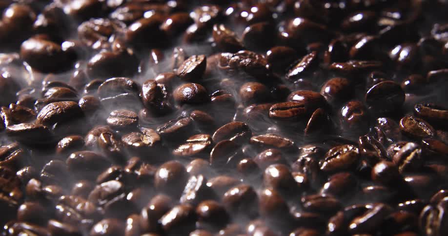 Steam rises and swirls above freshly roasted coffee beans