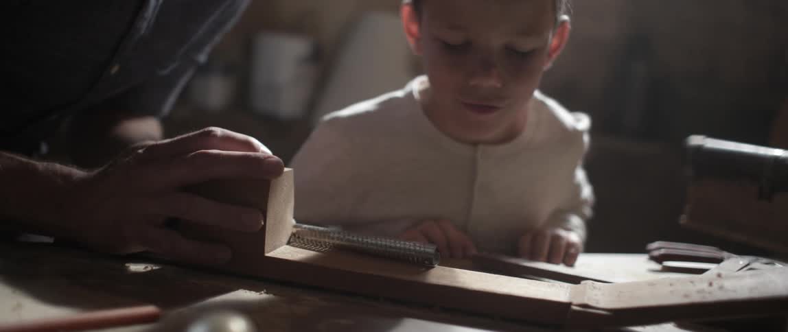 A boy blows wood shavings from a piece of wood