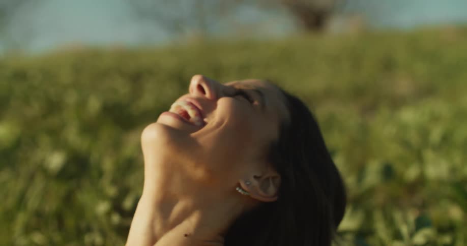 A woman laughs while in a field of vegetation during the day