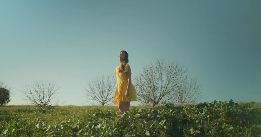 A woman in a yellow dress stands up from sitting in a open field