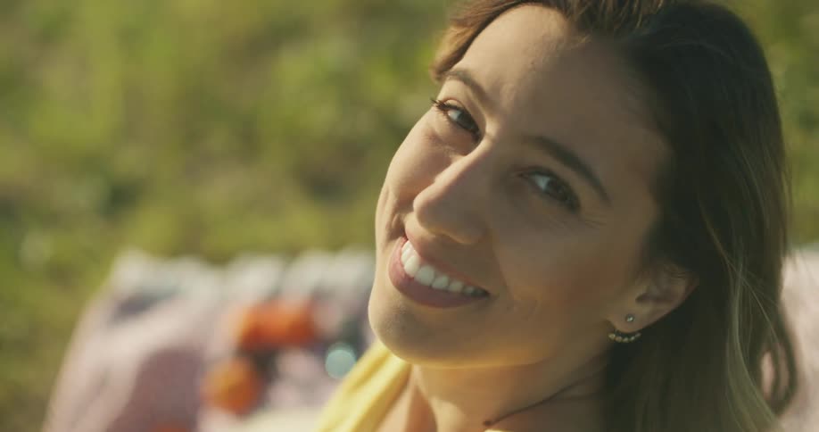 Woman sits on a blanket smiling at camera while the wind blows her hair on a sunny day