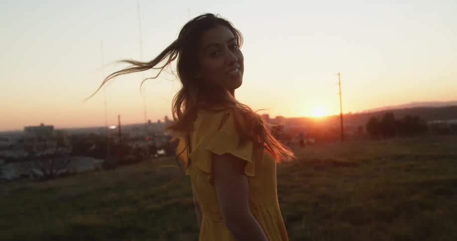 A woman smiles as she looks back and tosses her hair while walking at sunset